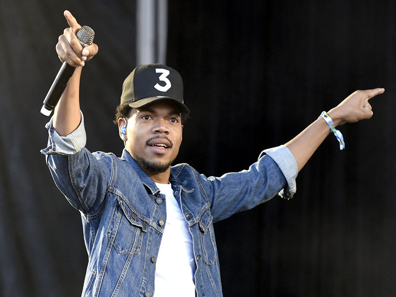 Clad in a jean jacket and white tee, Chance holds his hands out extended with the microphone © Pop Sugar